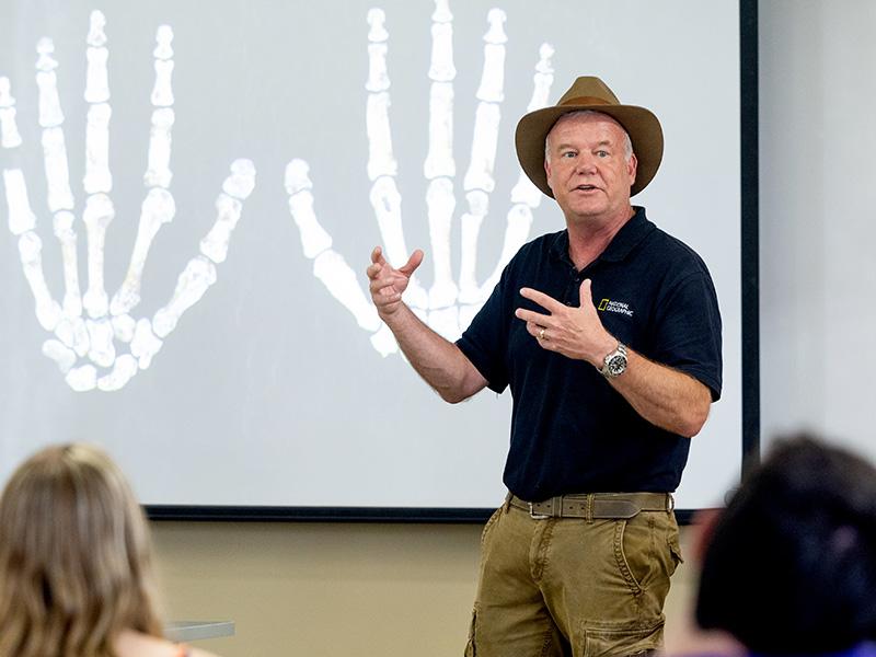 
Paleoanthropologist Lee Berger in front of a photo of Homo naledi hand specimens
